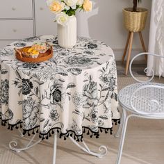 a table topped with a white vase filled with flowers next to a basket of fruit