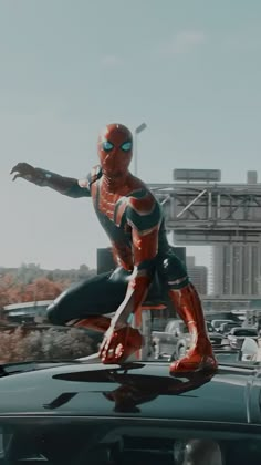 a spider - man standing on the hood of a car