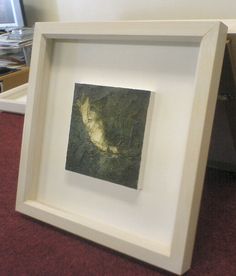 a white frame with a painting in it on top of a red carpeted floor