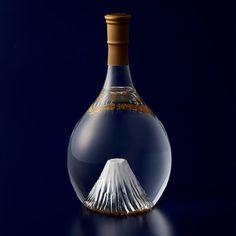 a glass bottle with a mountain in it on a blue tableclothed surface and dark background