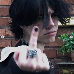 a man with black hair and piercings making the middle finger sign while standing in front of a brick wall