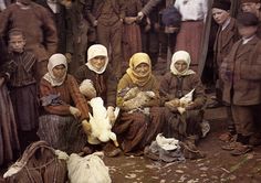 an old photo of women and children with chickens in front of them, all wearing headscarves