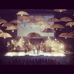 people standing on stage with umbrellas in the air and lights shining from above them