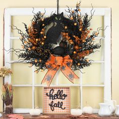 a halloween wreath on a window sill in front of a sign that says hello fall