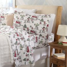 a bed covered in white and red sheets with christmas decorations on it, next to a night stand