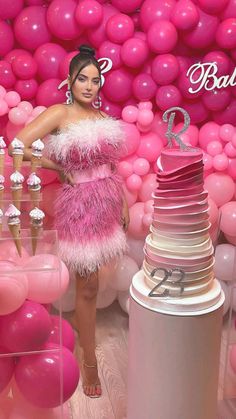 a woman standing next to a cake in front of pink balloons and desserts on display