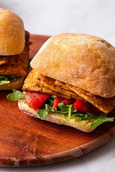 two sandwiches sitting on top of a wooden cutting board next to each other with lettuce and tomatoes