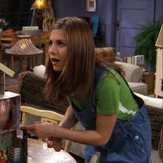 a woman in overalls is looking at an object on a table and pointing to it