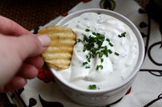 a hand holding a cracker over a bowl of white sauce and sour cream dip