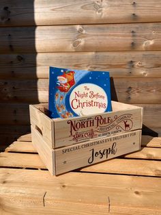 a wooden box with christmas cards in it on top of a wood table next to a fence