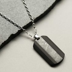 Our Meteorite and Carbon Fibre Dog Tag Necklace is a little piece of outer space you can wear on the daily. An out-of-this-world gift for the ones in your life who loves space. This dog tag necklace is styled with carbon fibre for a modern take on meteorite jewellery. Over 100,000 years ago, a handful of these mysterious Muonionalusta meteorites impacted earth. Searches for the impact crater from the original shower have been in vain; the site where these specimens are found is in a remote area of northern Sweden, is it presumed they were carried there by glaciers. Our Meteorite and Carbon Fibre Dog Tag Necklace comes in a elegant textured presentation box complete with information card and certificate of authenticity. The meteorites are not only extremely rare, they are almost always buri Everyday Black Engraved Necklaces, Everyday Black Engraved Necklace, Black Stainless Steel Jewelry For Everyday Use, Everyday Black Stainless Steel Jewelry, Nickel-free Stainless Steel Dog Tag, Black Laser Engraved Necklace As Gift, Black Laser Engraved Necklaces For Gifts, Black Laser Engraved Necklace For Gifts, Laser Engraved Black Necklaces For Gifts