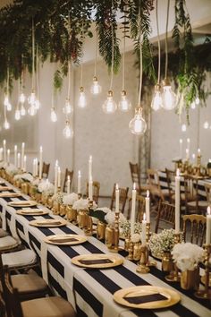 a long table with black and white striped runneres, gold place settings and hanging chandeliers