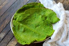 a bowl filled with green leafy food on top of a wooden table next to a white towel