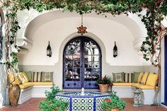 an outdoor area with potted plants, benches and a fountain in front of the door