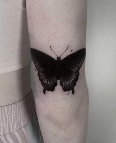 a black butterfly tattoo on the arm