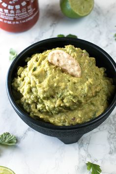 guacamole in a black bowl next to limes and ketchup