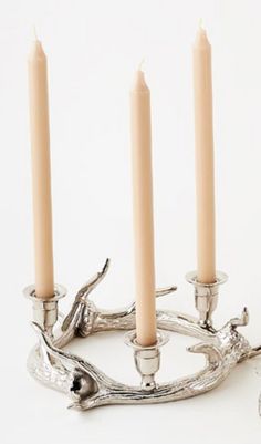 three candles are placed on a branch with two silver candelabra holders in the background