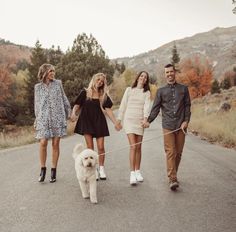 three people and a dog are walking down the road