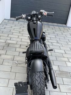 a black motorcycle parked in front of a garage door with the handlebars down