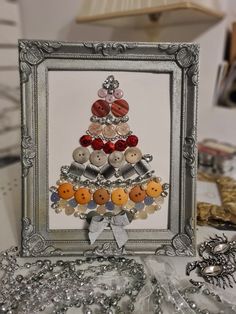 a christmas tree made out of buttons in a silver frame on top of a table