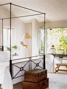 a bedroom with a canopy bed next to a white table and two brown trunks on the floor