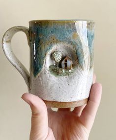 a hand holding a ceramic mug with a house on it