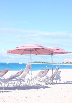 lounge chairs and umbrellas on the beach with blue water in the backgroud