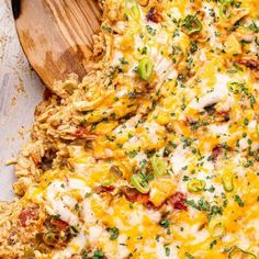 a casserole dish with meat, cheese and vegetables in it next to a wooden spoon