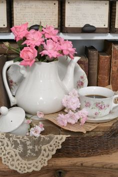 pink flowers are in a white tea pot on a table next to some old books