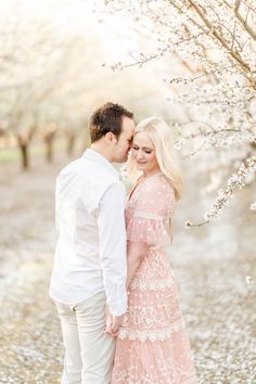 a man and woman standing next to each other under cherry blossom trees