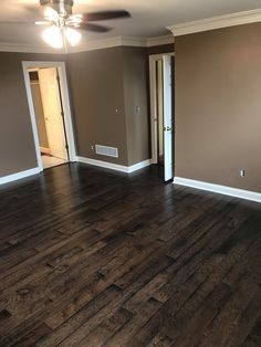 an empty living room with hard wood flooring and ceiling fan in the center area