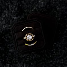 two rings sitting on top of each other in a black velvet box with gold trim