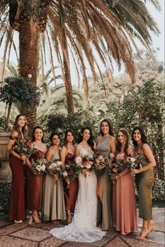 a group of women standing next to each other in front of a palm tree holding bouquets