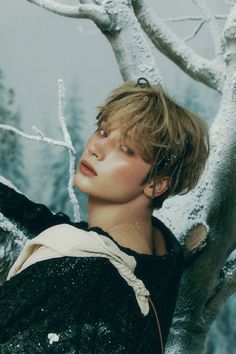 a young man standing next to a tree covered in ice and snow with his eyes closed