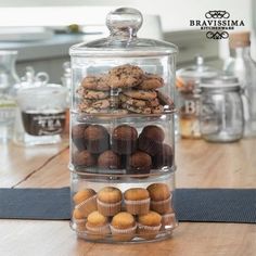 three tiered glass container filled with cookies and muffins on top of a wooden table