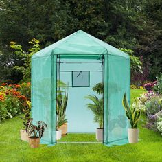 a small green house in the middle of a garden with potted plants and flowers