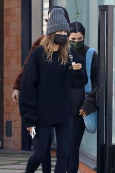 two women walking down the street wearing face masks and black leggings, with one woman looking at her phone