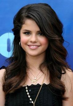 a beautiful young woman with long dark brown hair smiling at the camera and wearing a black dress