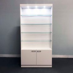 an empty white shelf with glass shelves and lights on top, against a gray wall