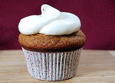 a cupcake with white frosting and sprinkles on top sitting on a wooden table