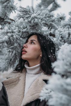 a woman standing in front of snow covered trees looking up at the sky with her eyes closed