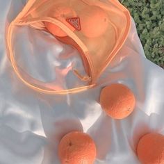 three oranges sitting on top of a white sheet next to an orange bag and some green plants