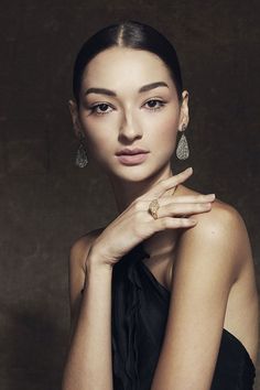 a woman in a black dress posing with her hands on her chest and wearing earrings