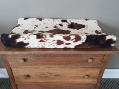 a brown and white cow print blanket sitting on top of a wooden dresser