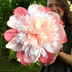 a woman holding a large pink and white flower in her right hand while smiling at the camera