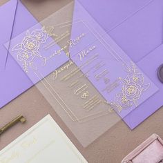 the wedding stationery is laid out on top of purple envelopes and gold foil