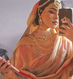 a woman in a bridal outfit is looking at her cell phone while wearing gold jewelry