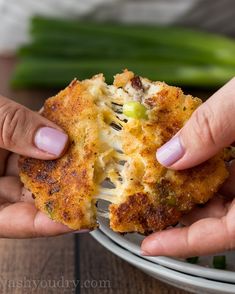 two hands holding a piece of food on a white plate with green onions and celery in the background