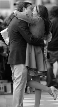 a man and woman kissing on the street in front of some people with their arms around each other