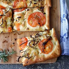 a square pizza with tomatoes and herbs on a cutting board